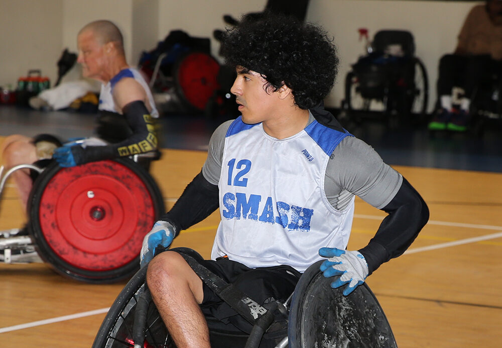 A young male athlete in a wheelchair, wearing a blue and white jersey with the number 12 and 